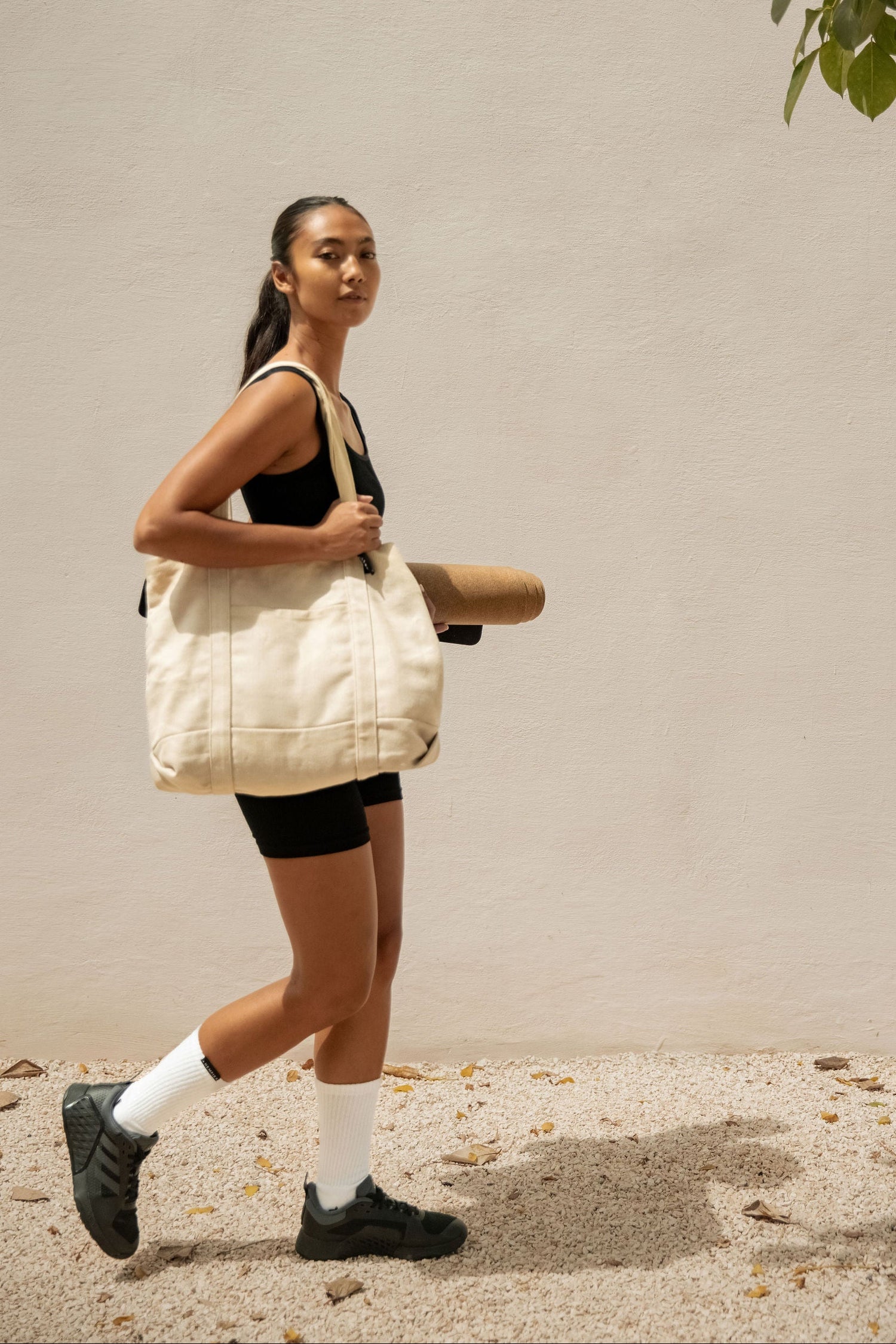 Woman walking outdoors with a beige tote bag, wearing athletic attire.